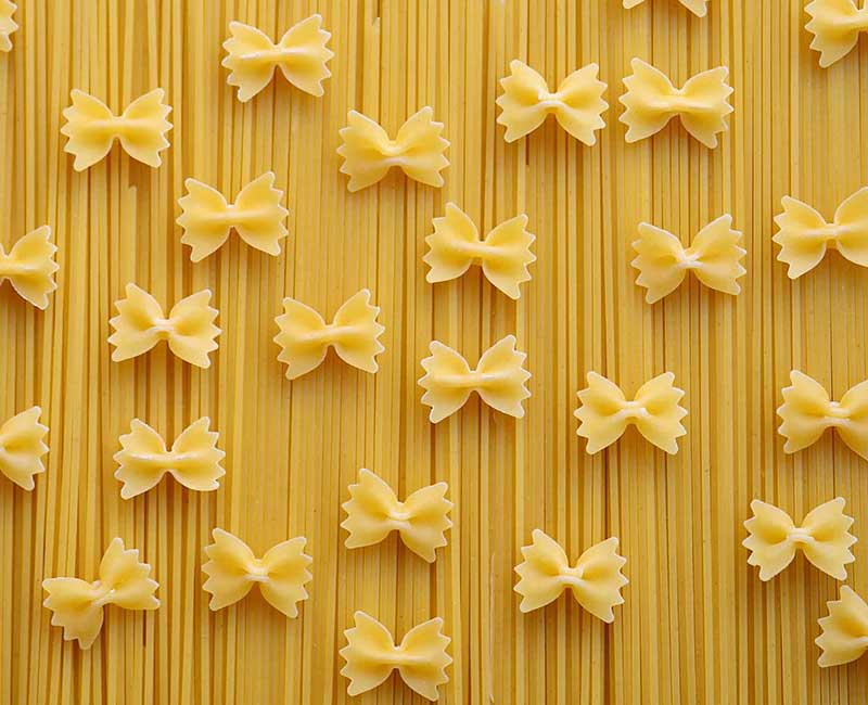 Pâtes longues et farfalle sèches disposées sur une surface