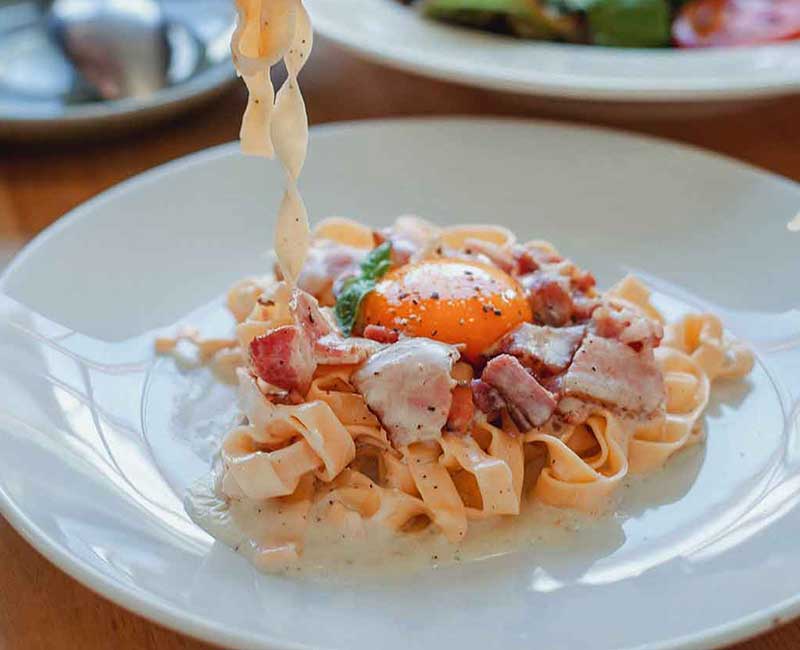 Fourchette soulevant des pâtes au-dessus d’une assiette avec des tomates