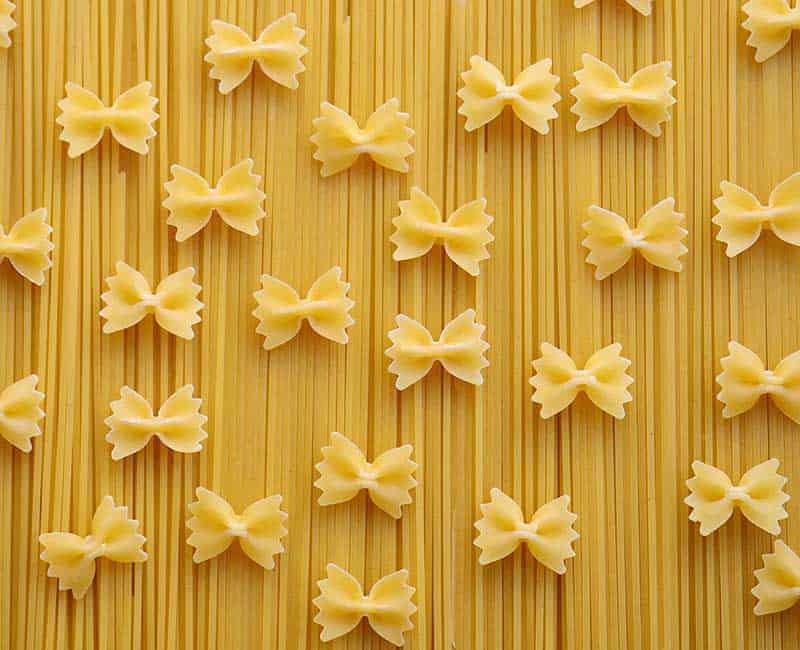 Pâtes longues et farfalle sèches disposées sur une surface