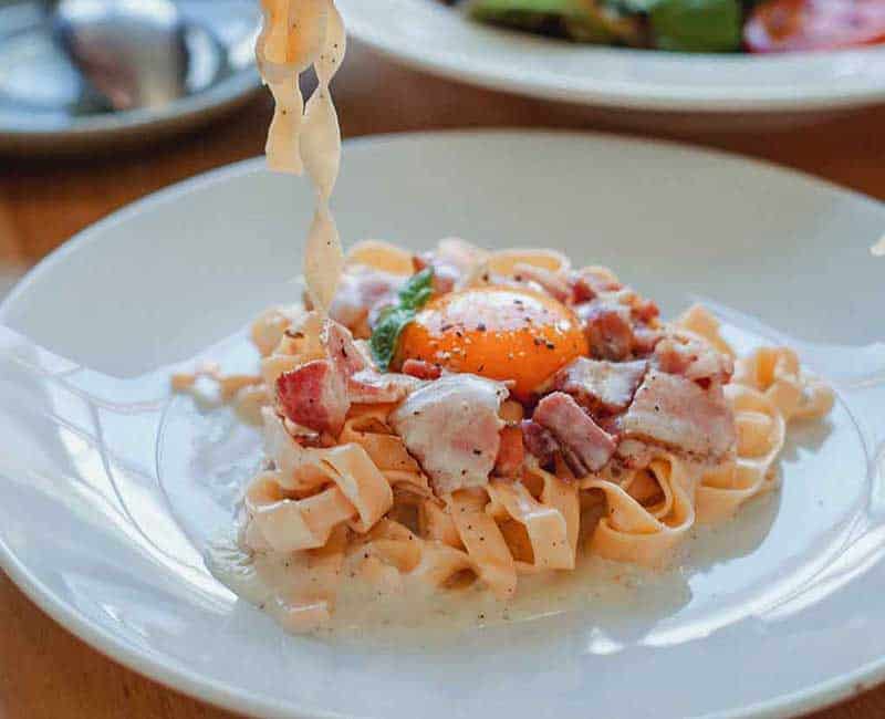 Fourchette soulevant des pâtes au-dessus d’une assiette avec des tomates