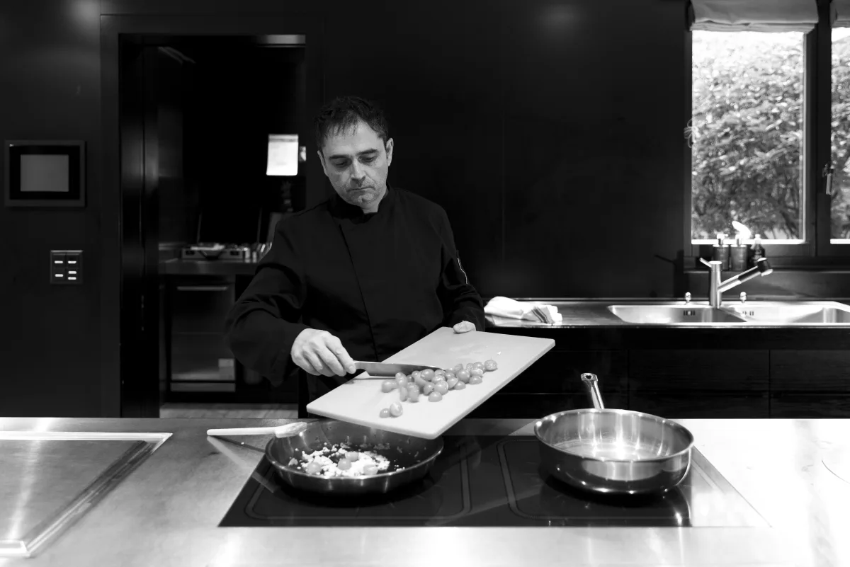 Bertrand Larzul ajoutant des tomates dans une poêle, photographie en noir et blanc.
